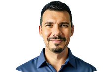 Man with short dark hair and a trimmed beard smiling, wearing a blue collared shirt.