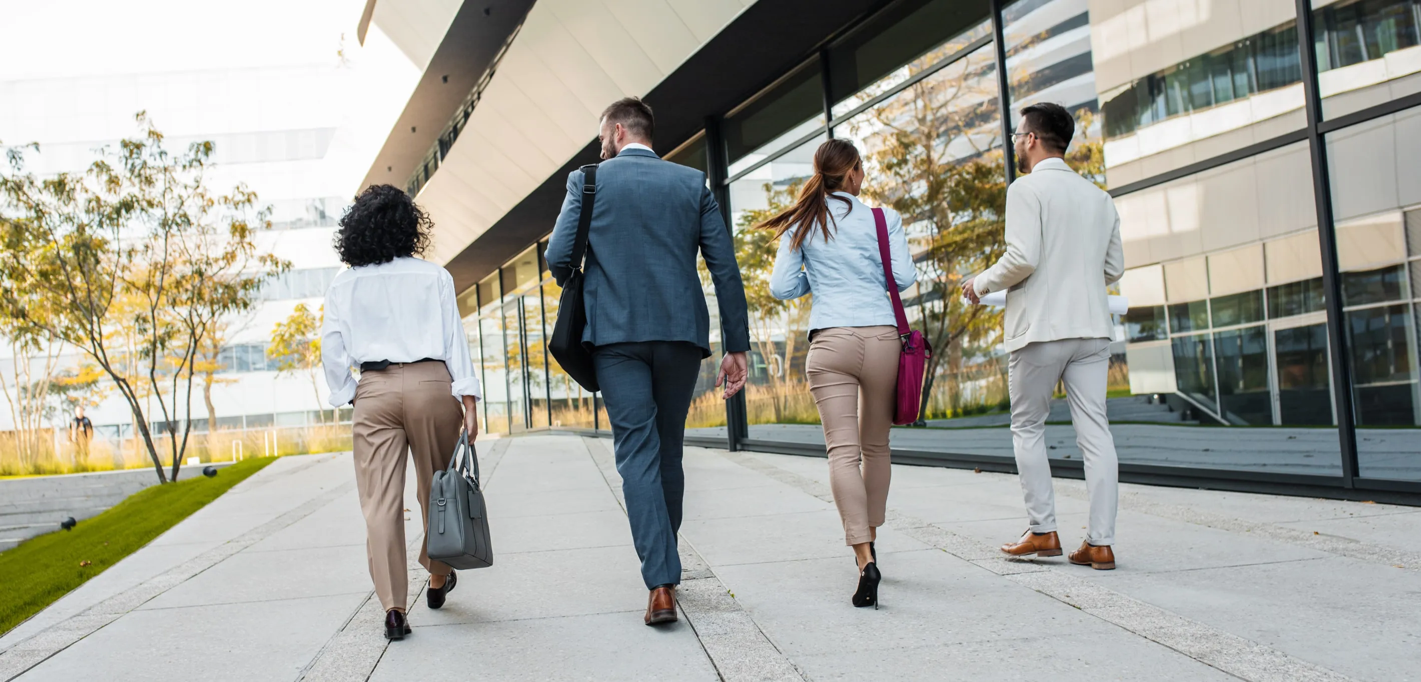 Four professionals walking outside a modern office building with glass walls.