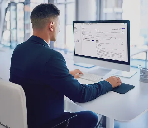 Man in a suit working on a desktop computer with a business application on the screen in a modern office.