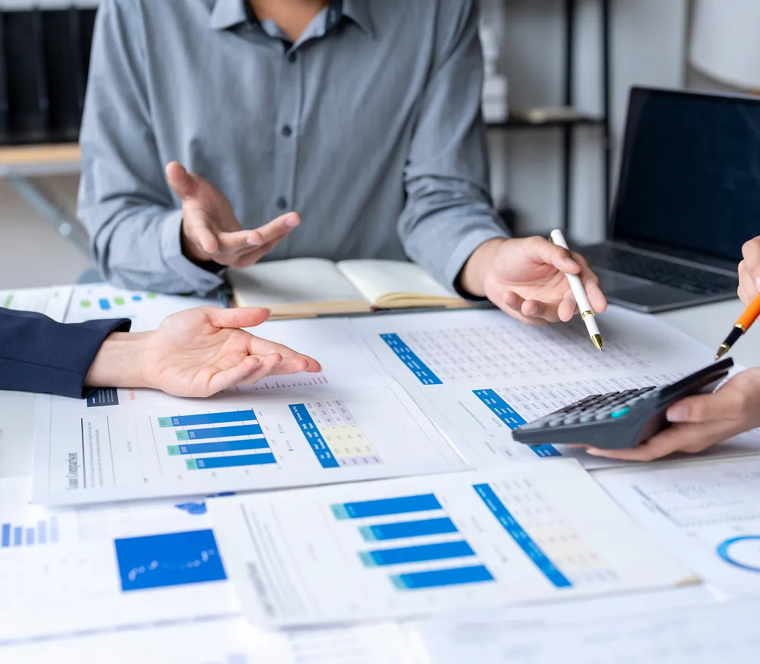 People discussing financial charts and data sheets while using a calculator at a desk.