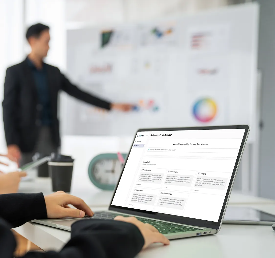 Person using a laptop displaying an FX Assistant dashboard in an office setting with a blurred colleague pointing at a whiteboard in the background.