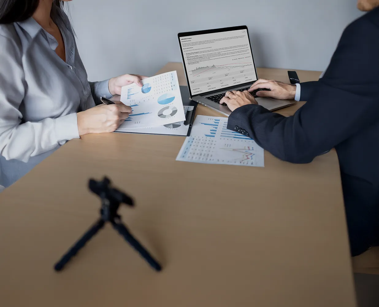 Two businesspeople reviewing charts and data reports with a laptop open displaying a graph on a wooden table.