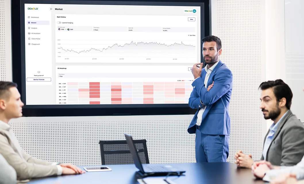 Businessman in a blue suit presenting financial market data on a large screen to colleagues in a conference room.