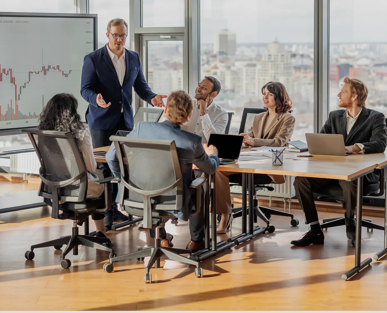 Businessman presenting financial data to a diverse group in an office with city view.