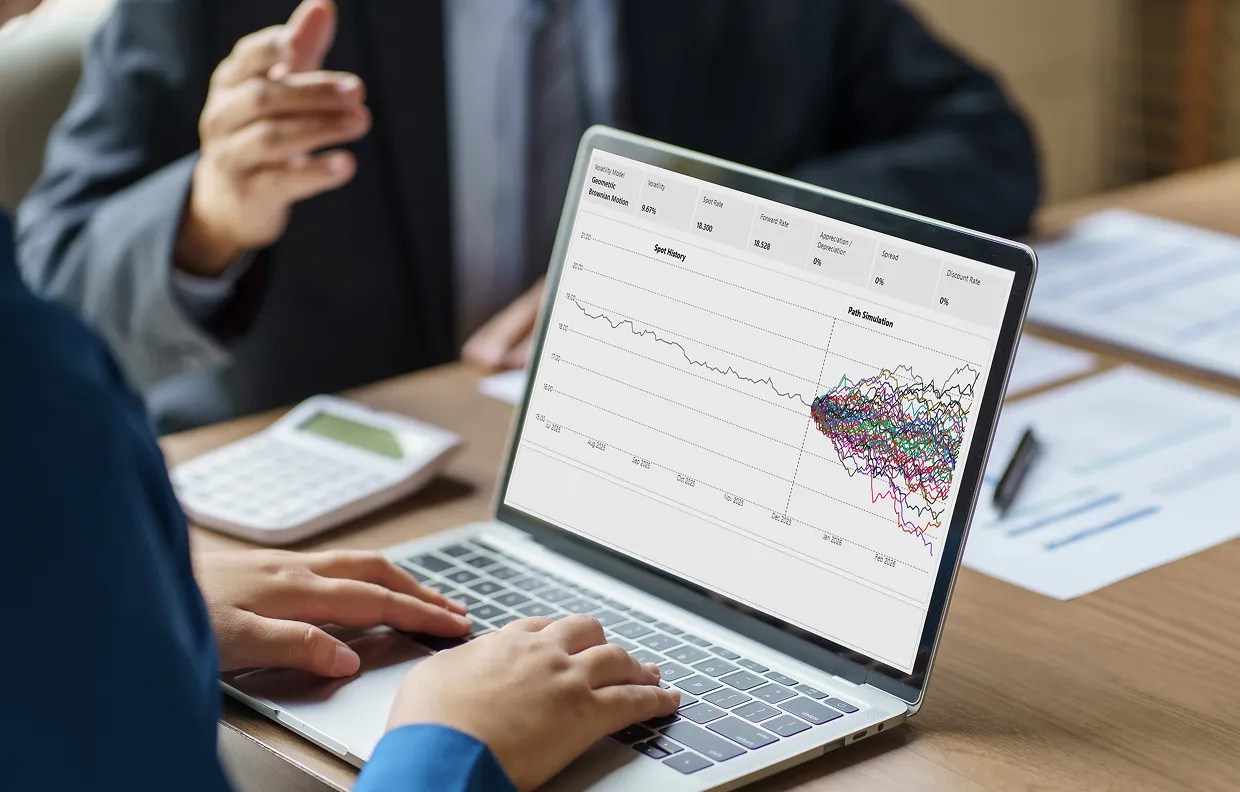 Person working on a laptop displaying a financial chart with spot history and multiple path simulations, while another person gestures in discussion.