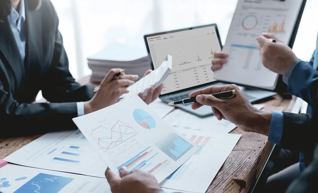 Business professionals analyzing financial charts and graphs on papers and a laptop during a meeting.