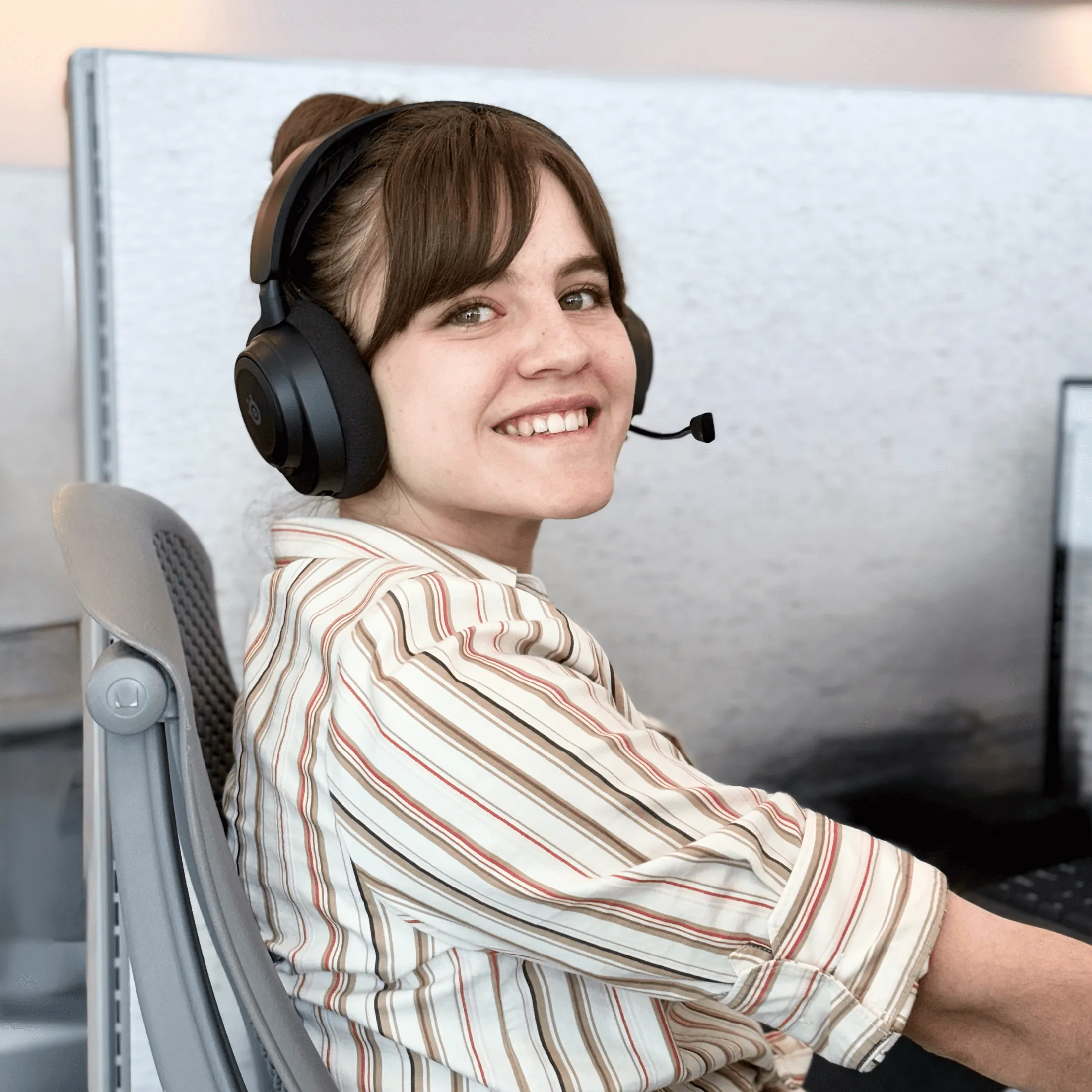 Young woman smiling while wearing a headset and working at a computer in an office.
