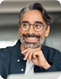 Smiling man with gray hair, beard, and glasses resting his chin on his hand.