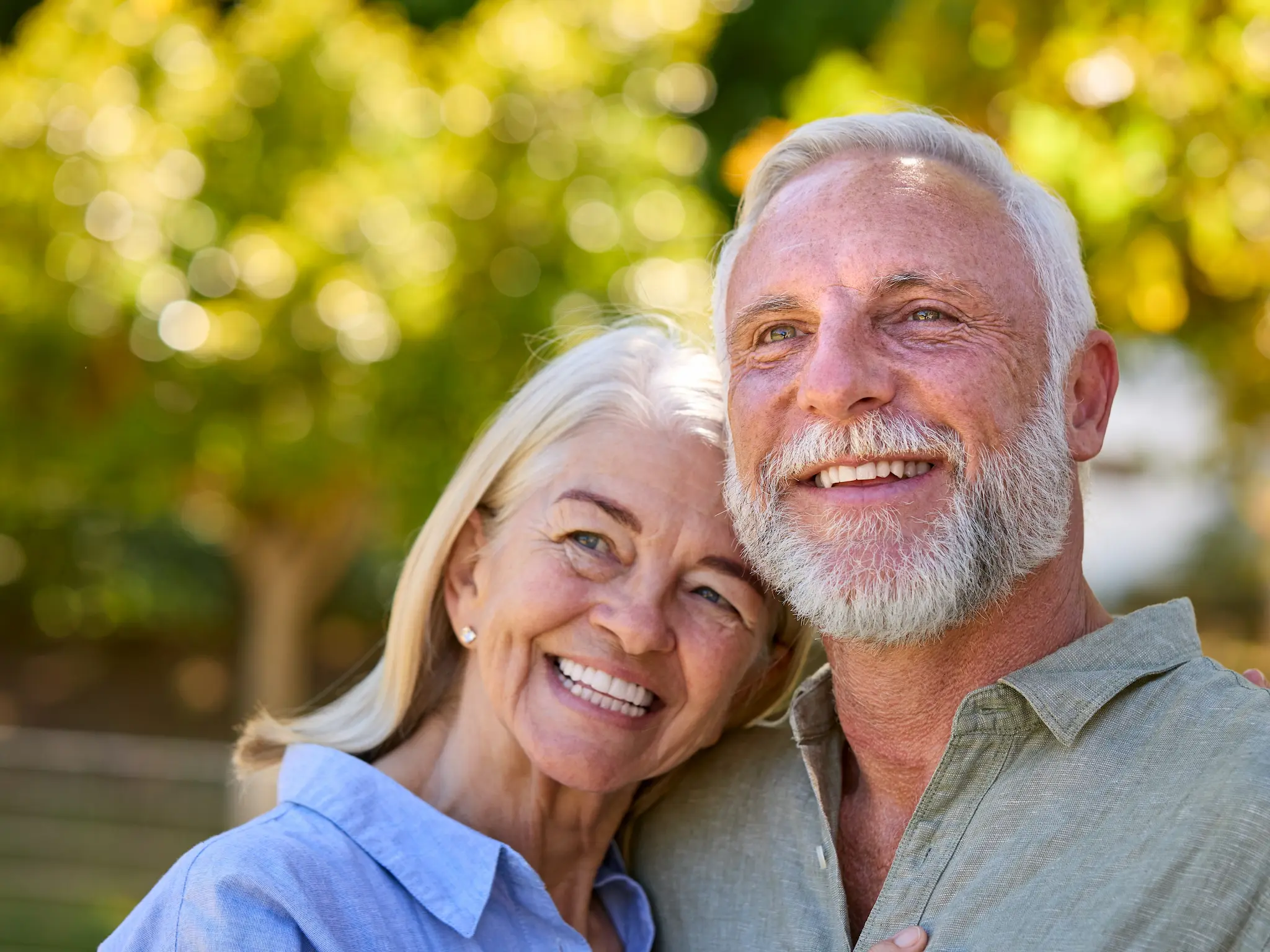 Smiling senior couple outdoors with greenery in the background.