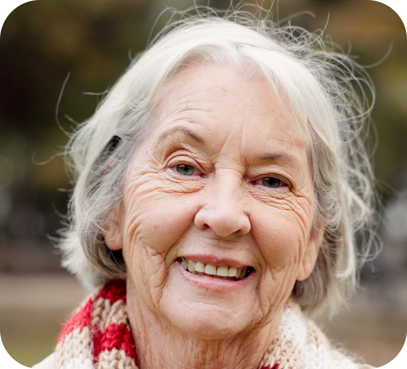 Smiling elderly woman with white hair wearing a red and beige knitted scarf outdoors.