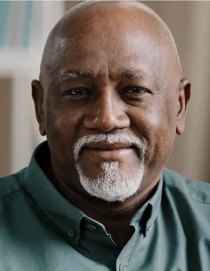 Smiling elderly man with bald head and white beard wearing a green shirt.