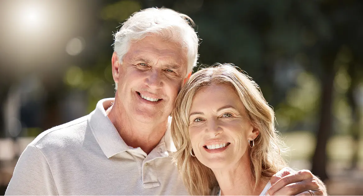Smiling senior couple outdoors with the man’s arm around the woman’s shoulder.