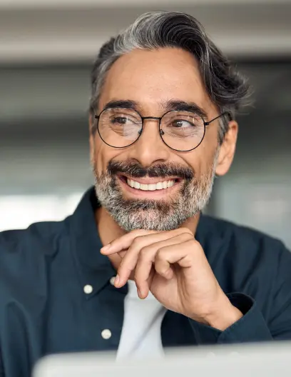 Smiling middle-aged man with gray hair, beard, and round glasses resting chin on hand.