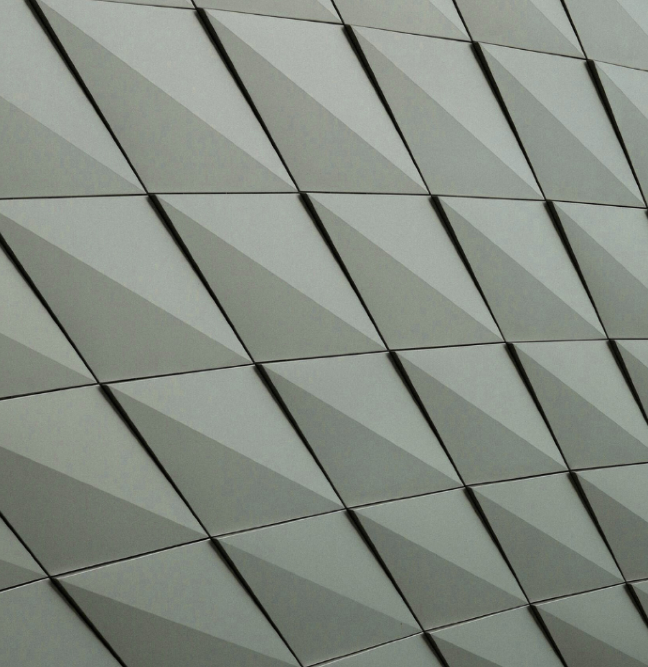 Close-up of a modern building facade featuring a repeating pattern of angular, three-dimensional triangular panels in shades of gray.