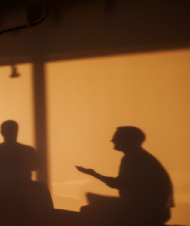 Shadows of two people against a wall, one person appears to be gesturing with their hand.