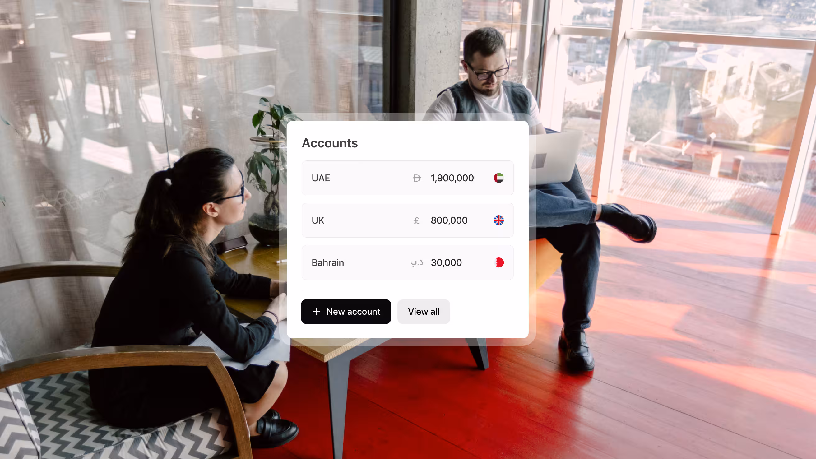 Two women smiling and talking near a glass door, with an overlay showing account balances for UAE, UK, and Bahrain.