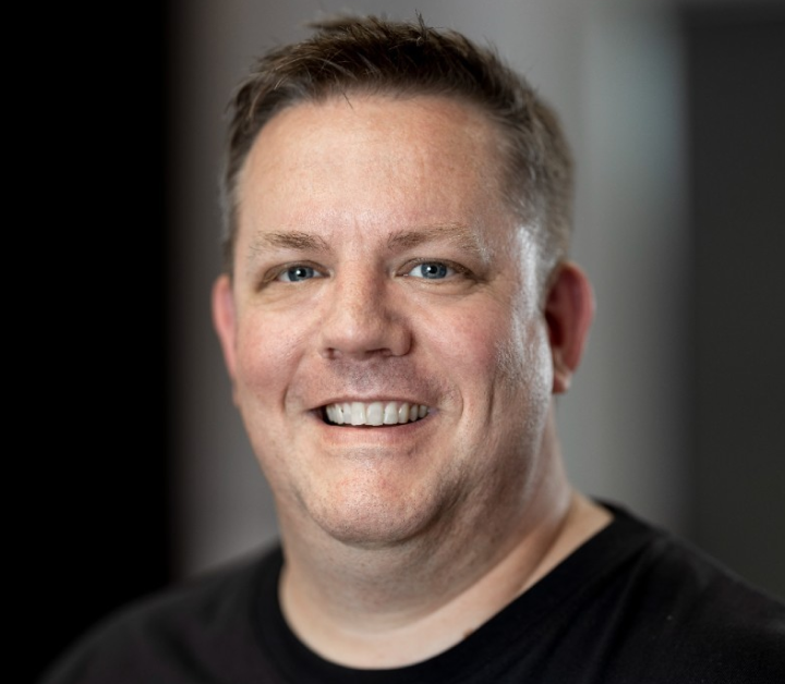 Smiling man with short brown hair and blue eyes wearing a black shirt.