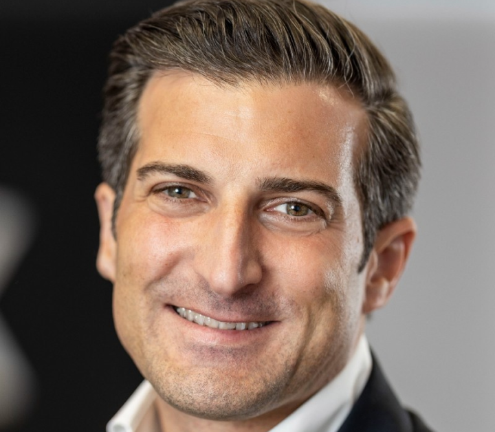 Smiling man with neatly styled brown hair wearing a white shirt and dark jacket.