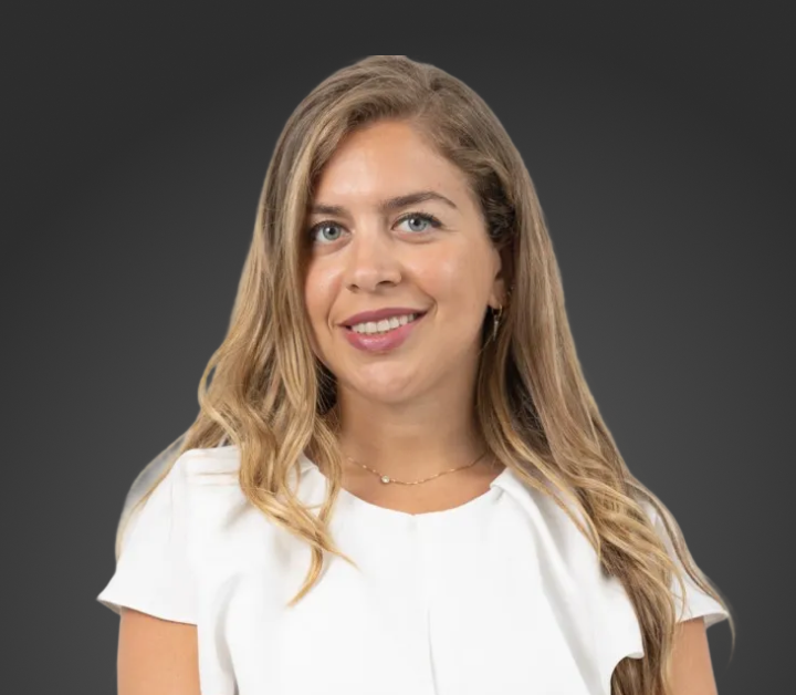 Smiling woman with long blonde hair wearing a white blouse against a dark gray background.
