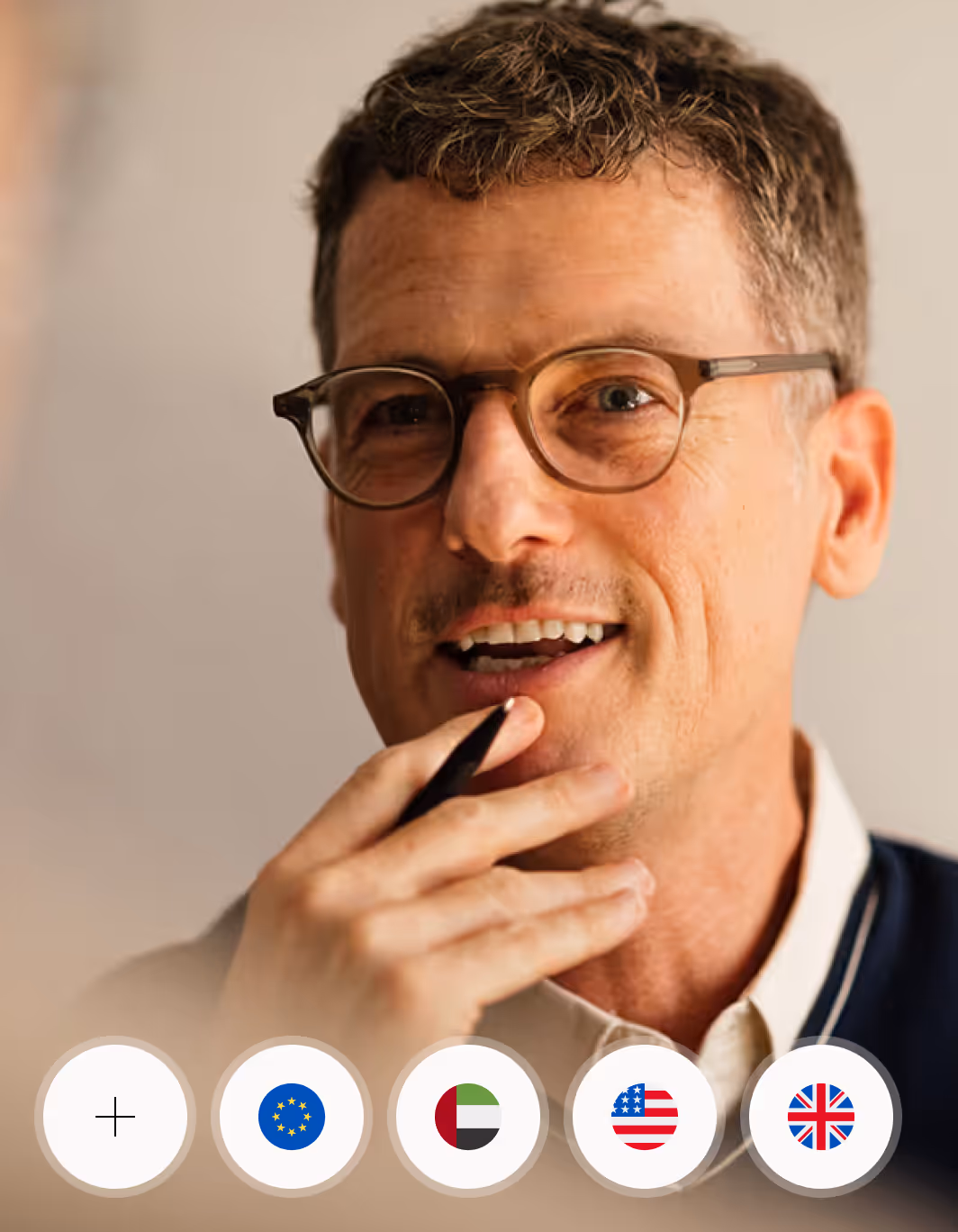 Middle-aged man with glasses holding a pen near his mouth, smiling thoughtfully.