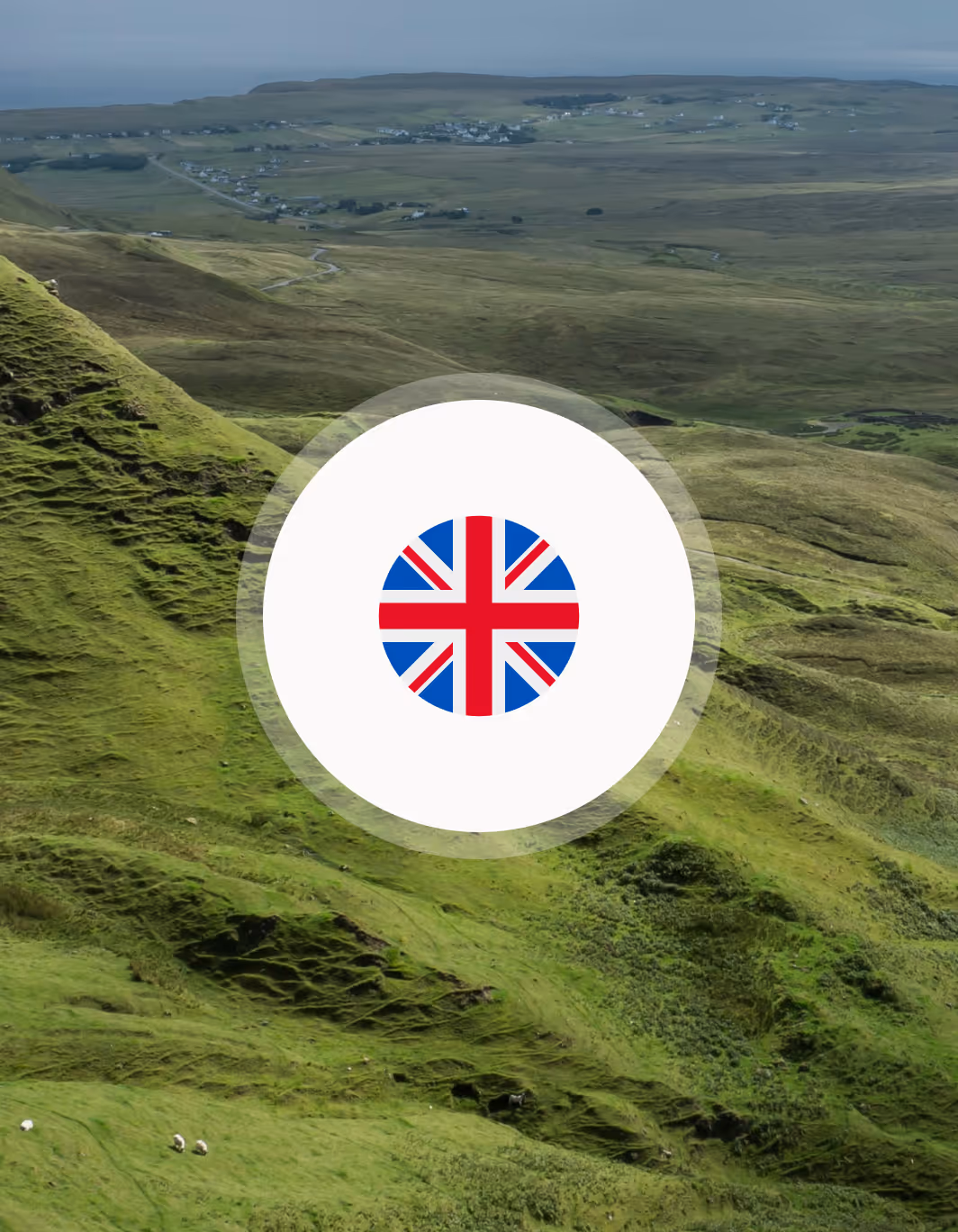 Aerial view of a green hilly landscape with scattered houses in the distance and a circular British flag icon in the center.