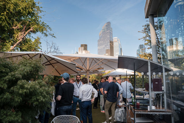Guests talking under parasols on a London rooftop terrace, City skyscrapers behind