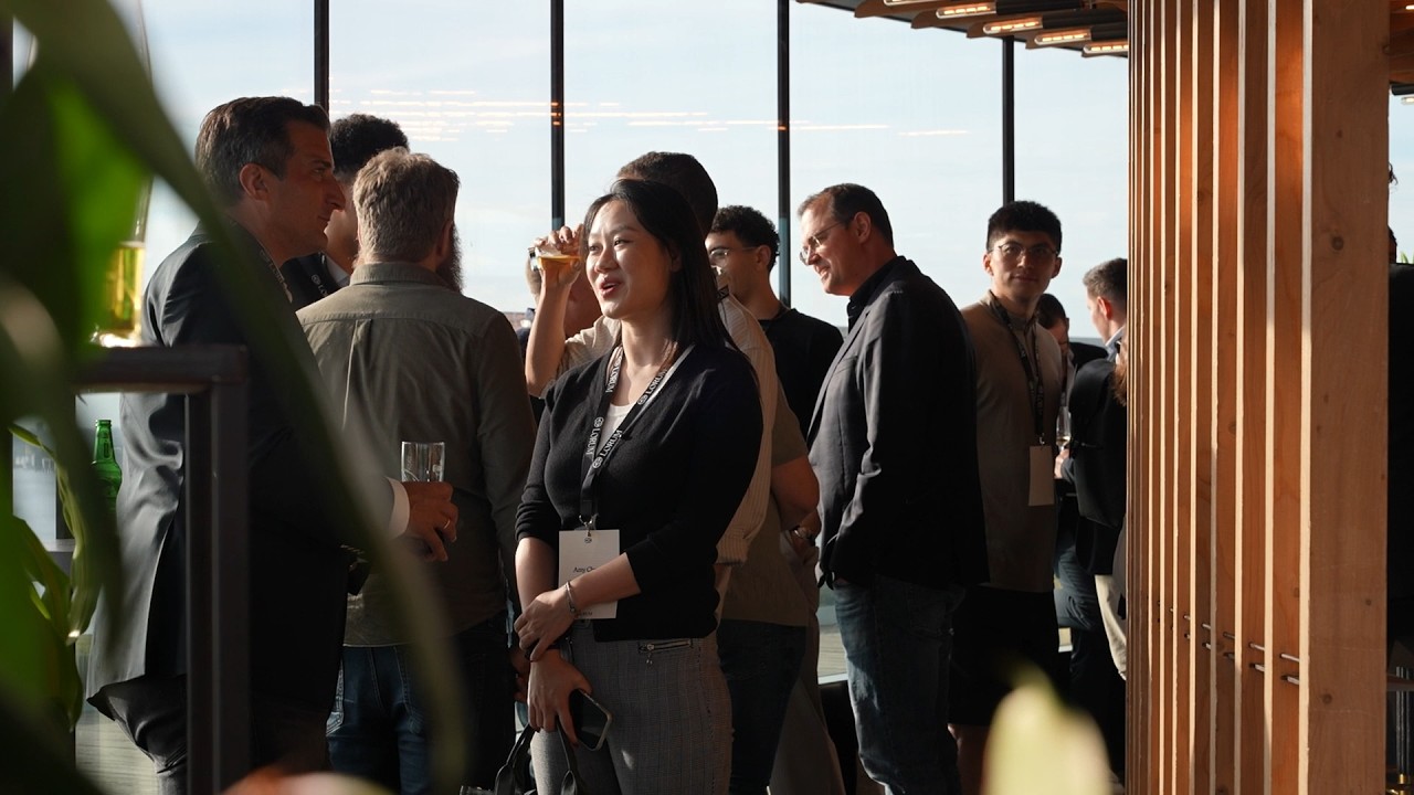 Guests with lanyards talking by the floor-to-ceiling windows of A'DAM Tower at the Amsterdam evening