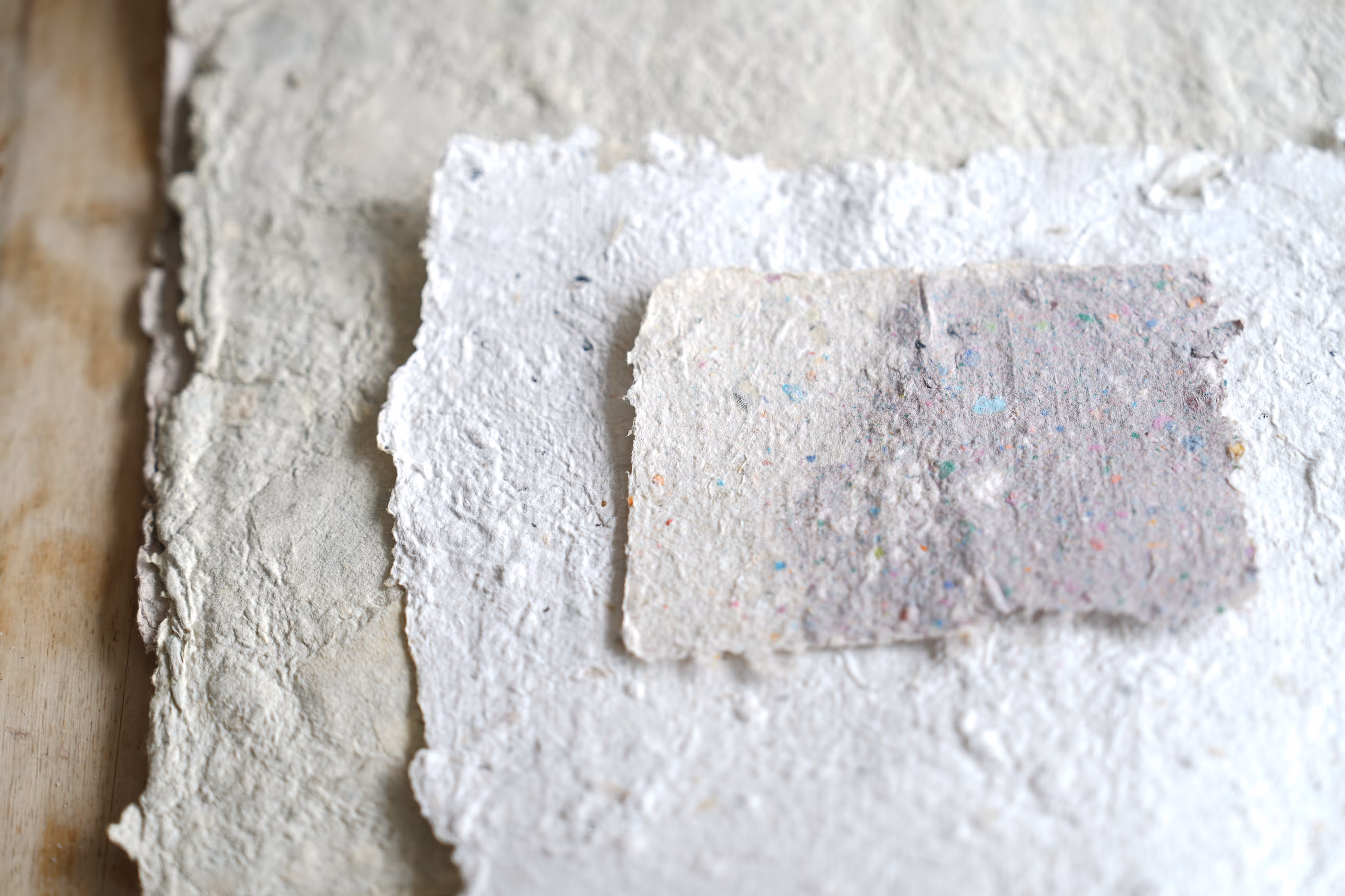 Gestapelde vellen gerecycled papier met een ruwe textuur op een houten oppervlak.