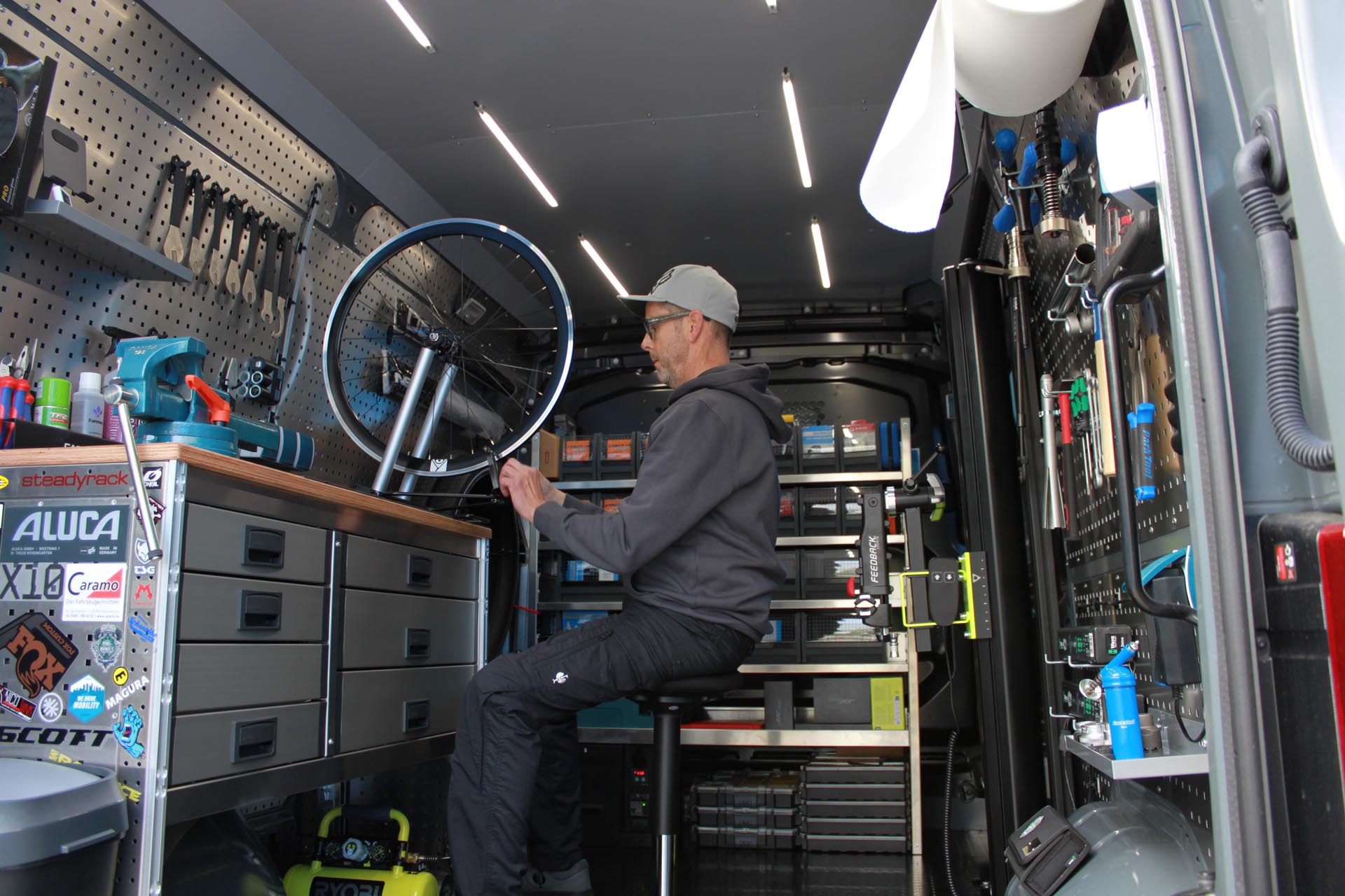 Ein Mann repariert ein Fahrrad in einem gut organisierten mobilen Werkstattwagen mit Werkzeugen und Ersatzteilen.