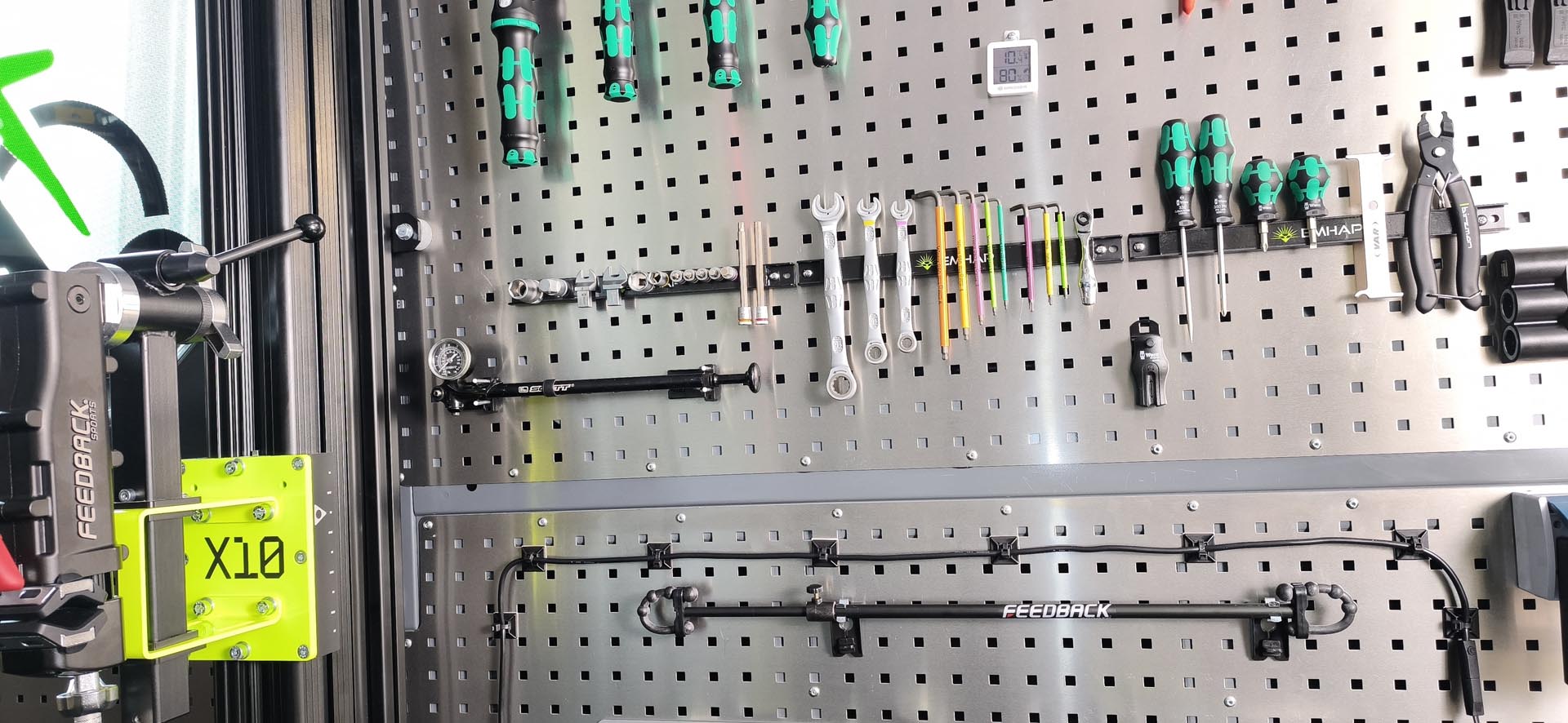 Wand mit verschiedenen Werkzeugen wie Schraubendrehern, Schlüsseln, Zangen und Hebeln, organisiert auf einer Lochtafel.