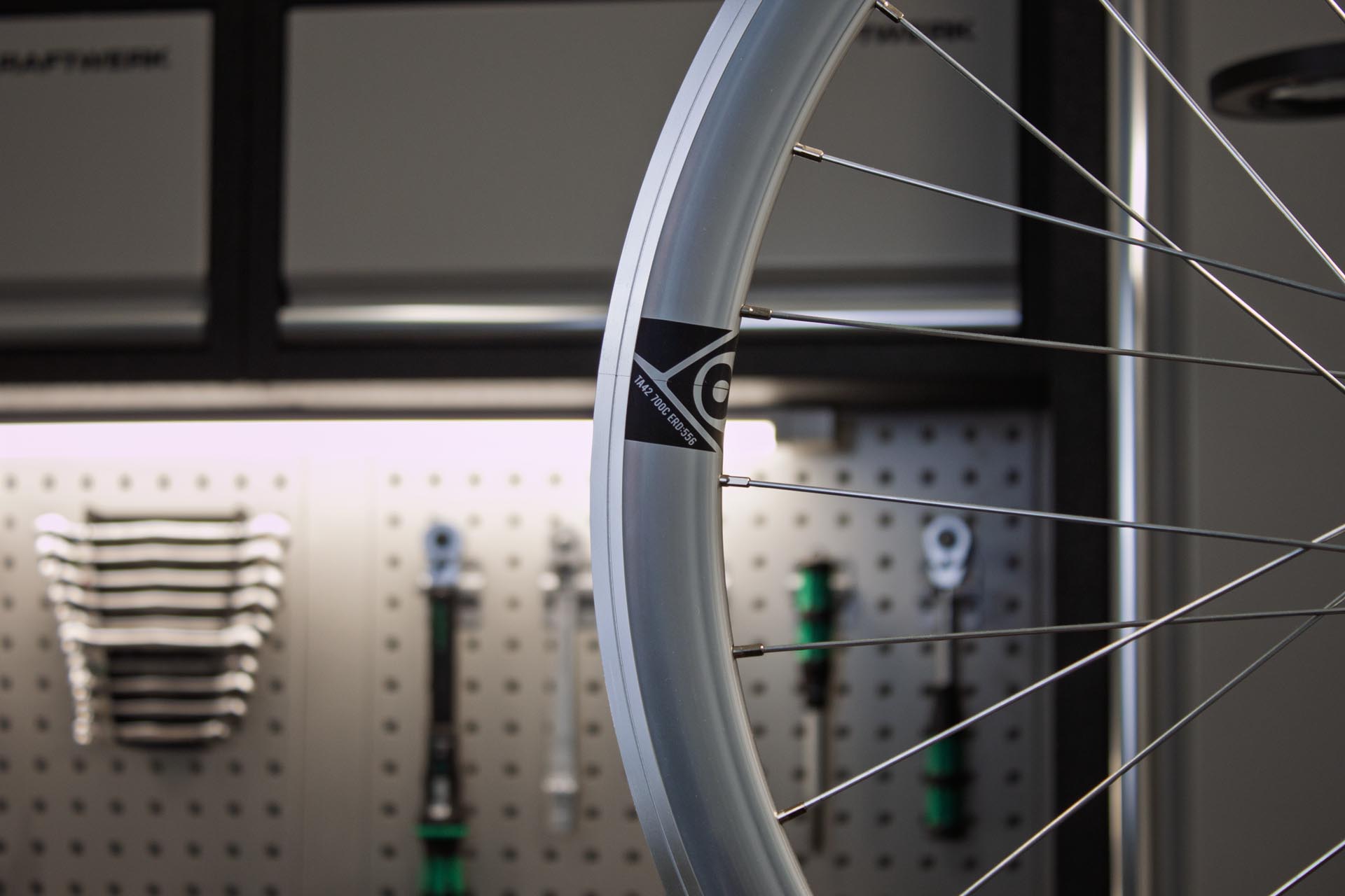 Nahaufnahme eines Fahrradreifens mit Speichen, im Hintergrund Werkzeuge an einer perforierten Wand.