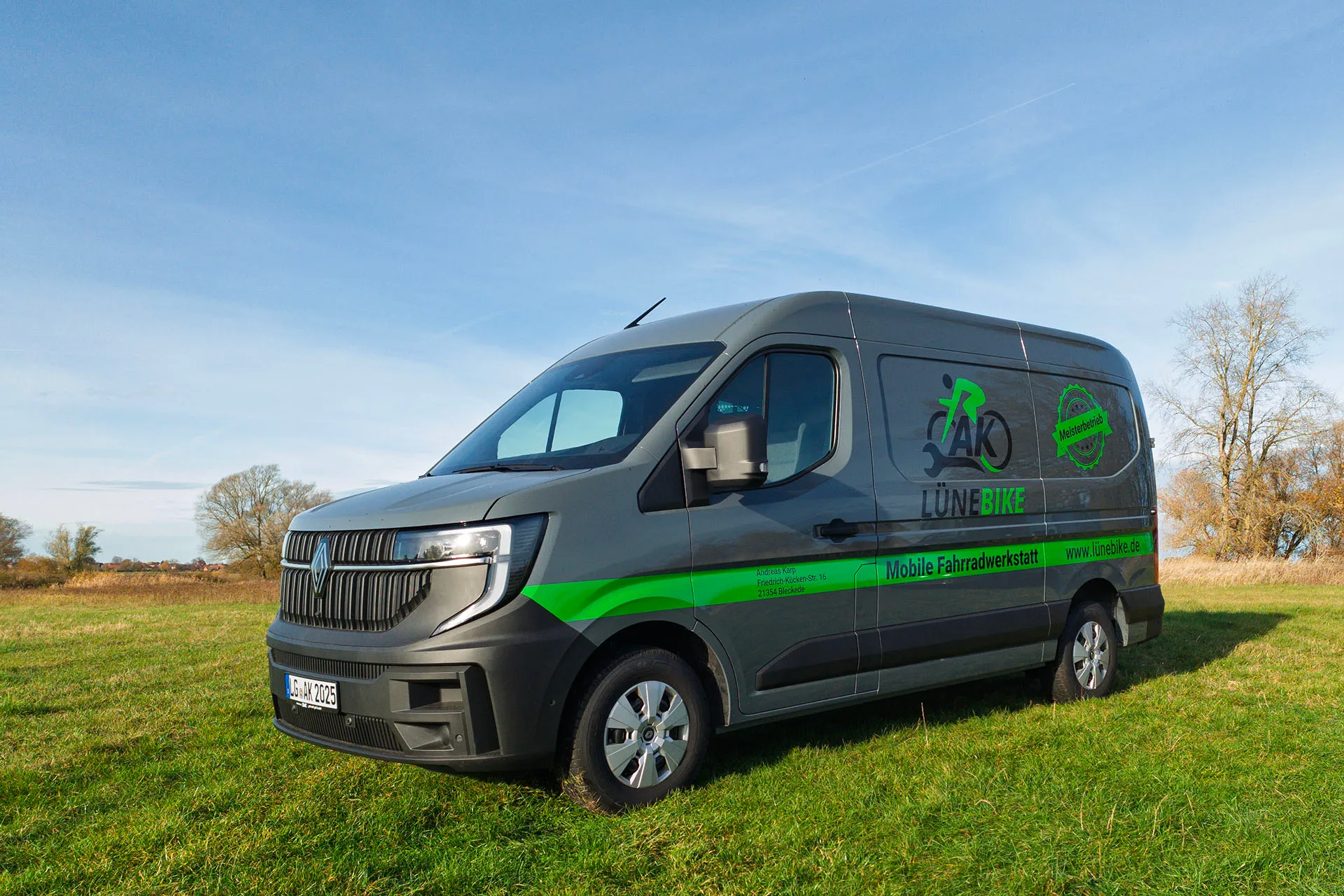 Grauer Transporter mit grünem Streifen im Feld, beschriftet mit LÜNEBIKE und Mobile Fahrradwerkstatt.