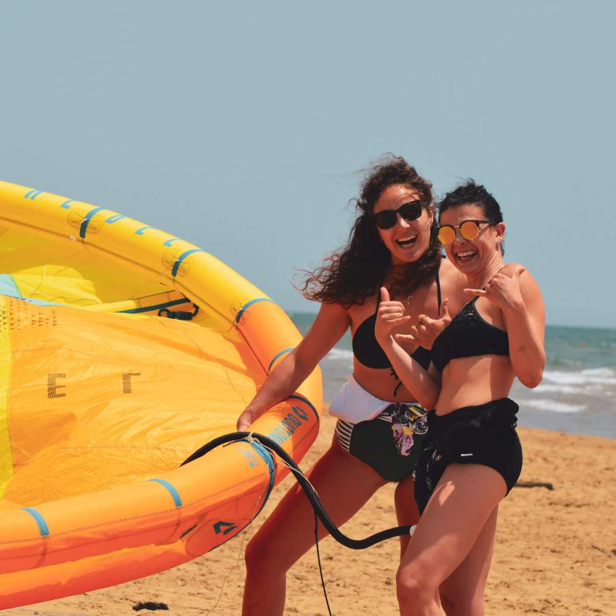 Two women preparing a kite for kitesurfing at Floripa Surf and Yoga House in Sicily, enjoying beach life and ocean adventure