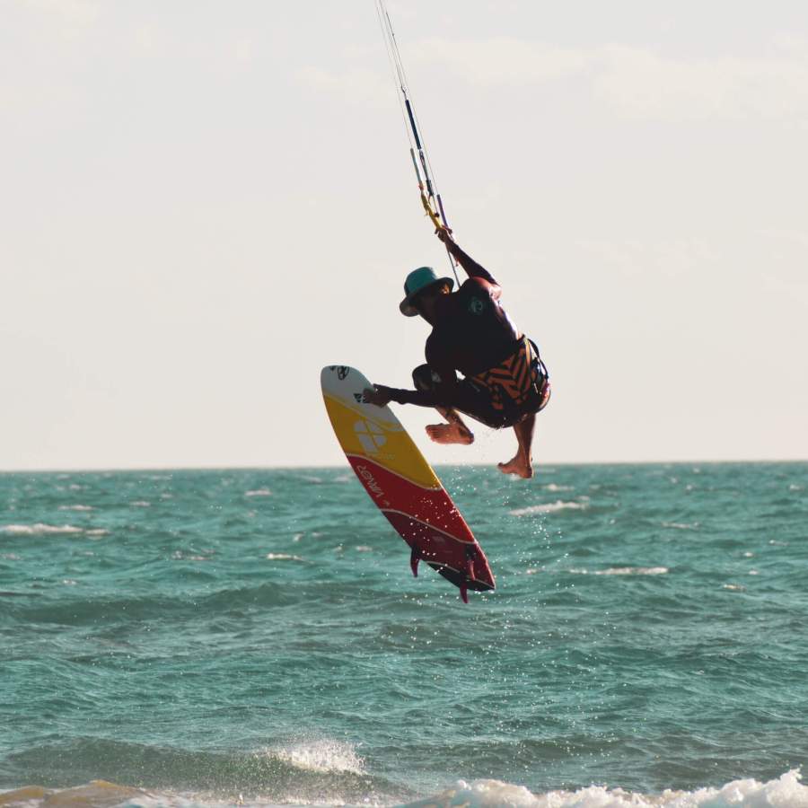 Kitesurfer performing an aerial maneuver on a directional board at Floripa Surf and Yoga House in Sicily, showcasing professional kitesurfing conditions