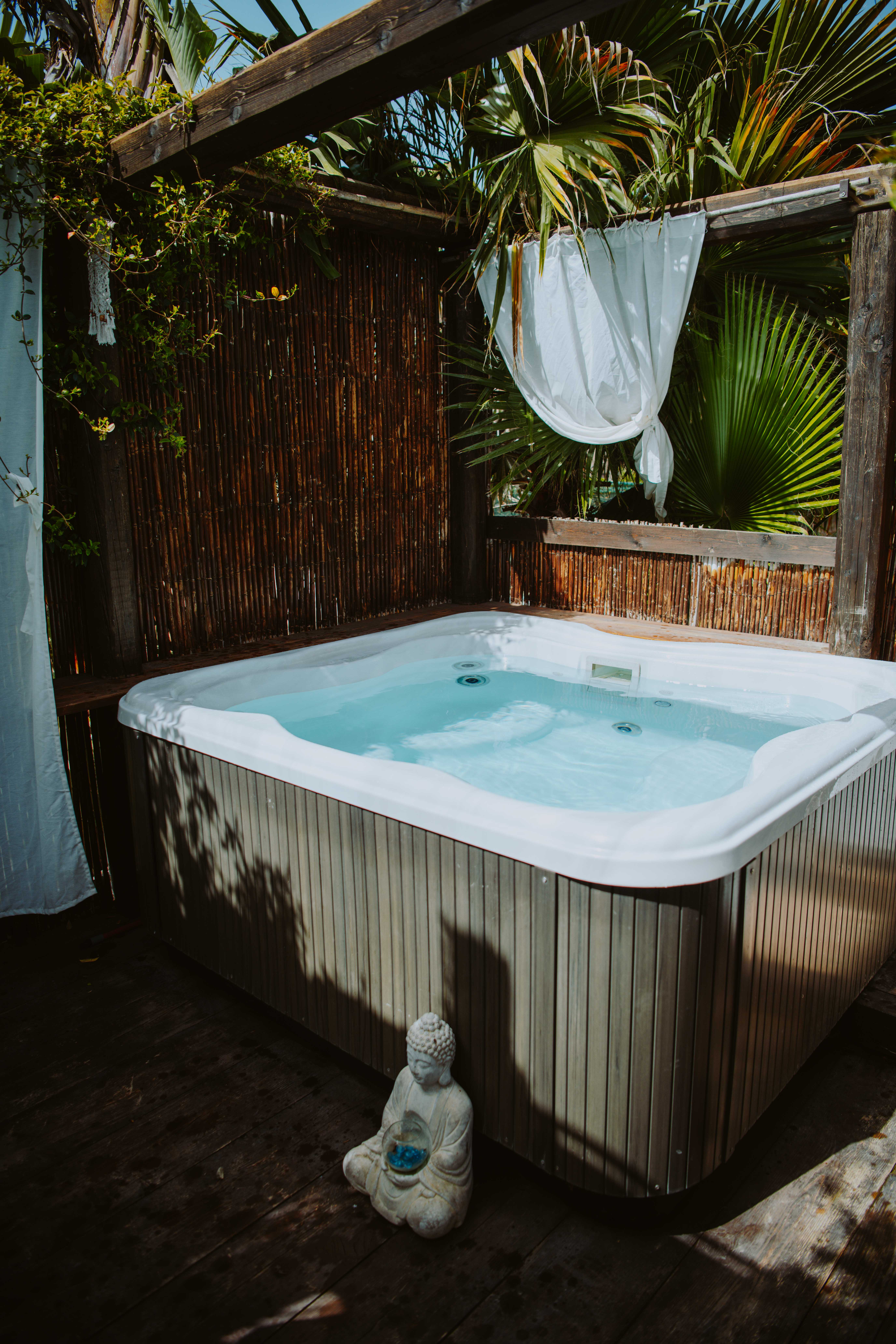 Outdoor jacuzzi at Floripa Yoga and Surf Retreat in Sicily, surrounded by tropical plants and a Buddha statue for a peaceful wellness experience