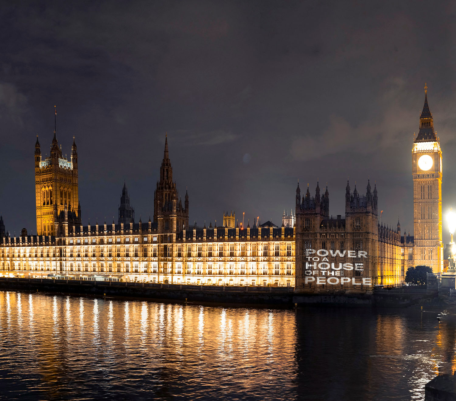 Parliament at night with a projection reading 'Power to a House of the People' shining over the Thames