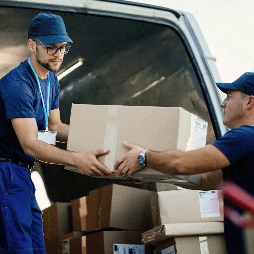 Zwei Lieferanten in blauer Arbeitskleidung übergeben sich ein Paket vor einem Lieferwagen mit weiteren Paketen.