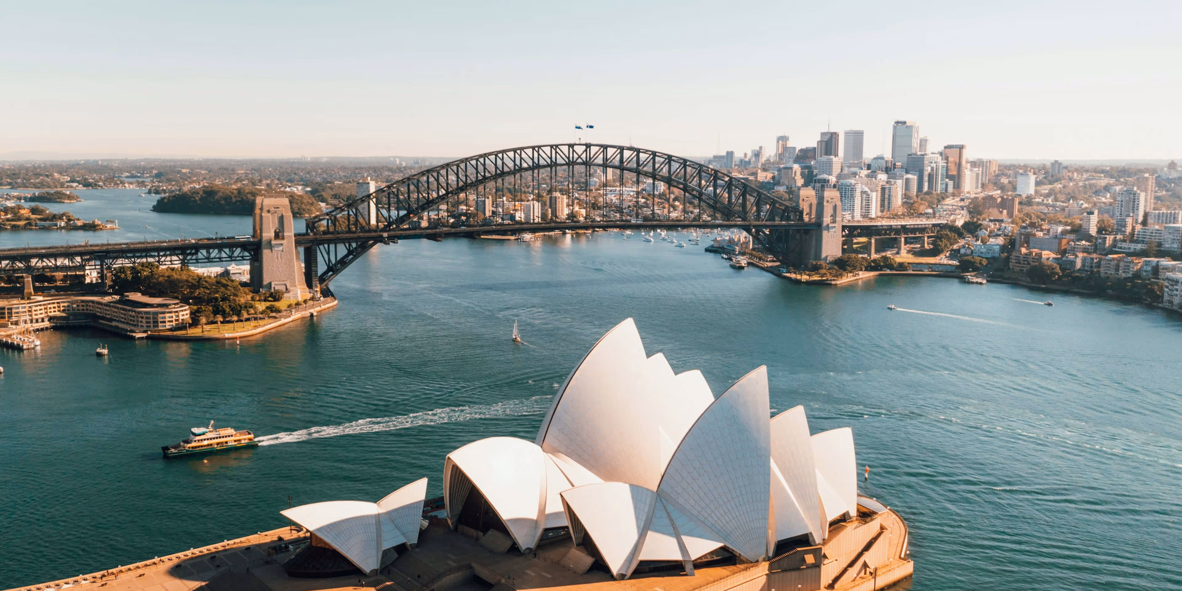 Aerial view of Sydney Opera House with Sydney Harbour Bridge and city skyline in the background.
