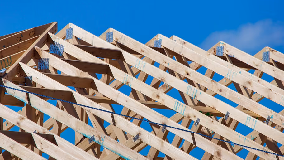 Close-up of wooden roof trusses under construction against a clear blue sky.