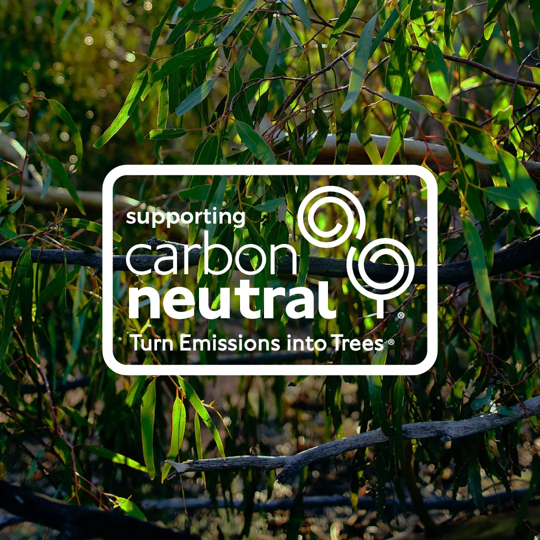Green leafy branches with sunlight filtering through, overlaid with white text and a logo reading: supporting carbon neutral Turn Emissions into Trees.