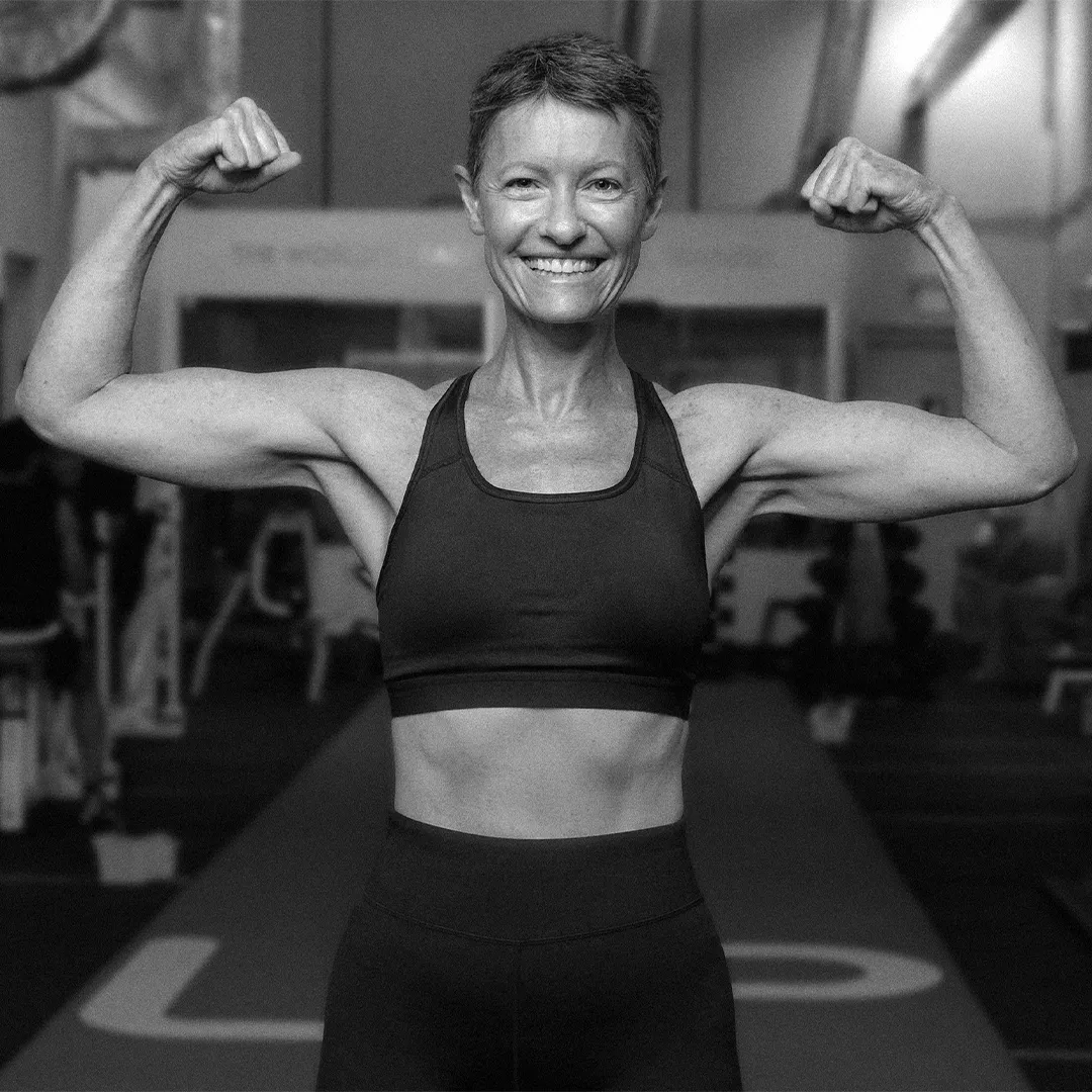 Smiling woman in athletic wear flexing her biceps in a gym.