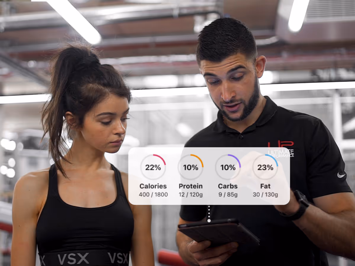 Fitness coach in black shirt showing nutrition data on a tablet to a woman in a black sports bra at the gym.