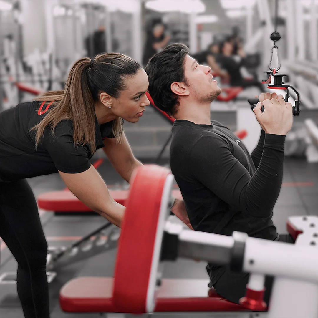 Female trainer assisting a man performing seated cable rows in a gym.