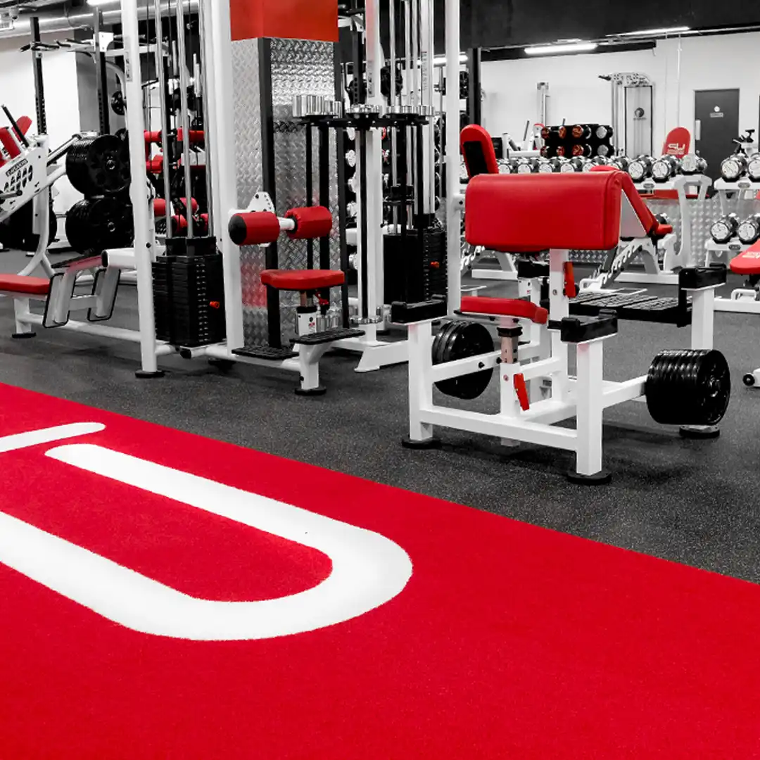 Modern gym interior with red and white weight machines and dumbbells on racks.