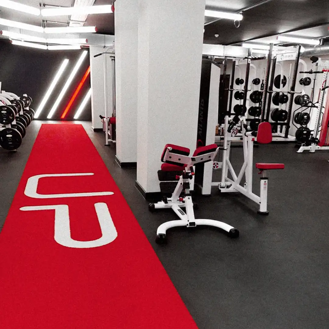 Modern gym interior with red carpet walkway, exercise machines, and weight racks.