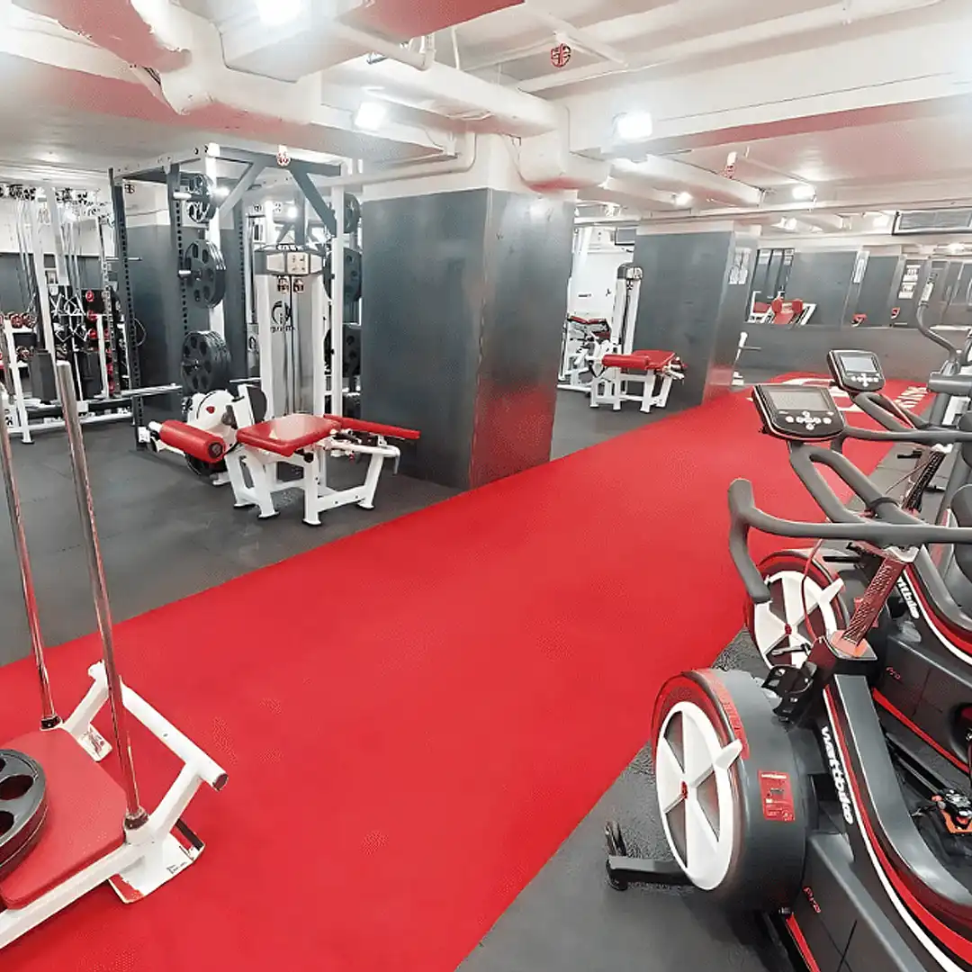 Modern gym interior with red exercise machines and a red carpeted walkway.