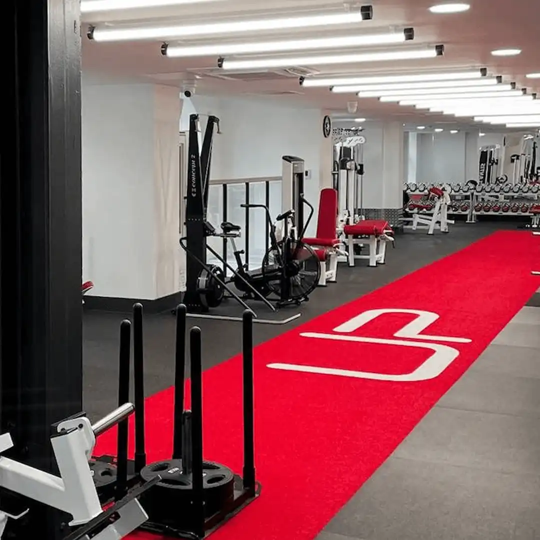 Modern gym with red carpeted track, exercise machines, weights, and black and white workout equipment.