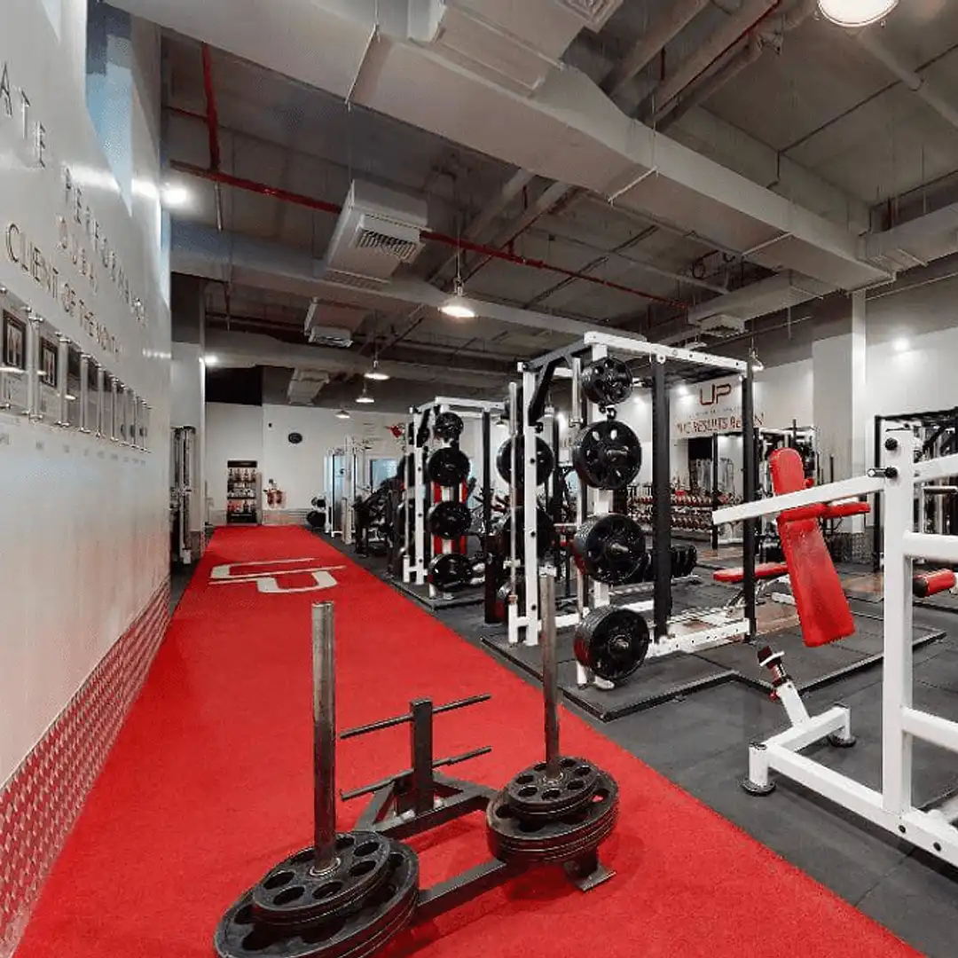 Modern gym interior with weightlifting stations, red padded benches, and a red carpeted track.