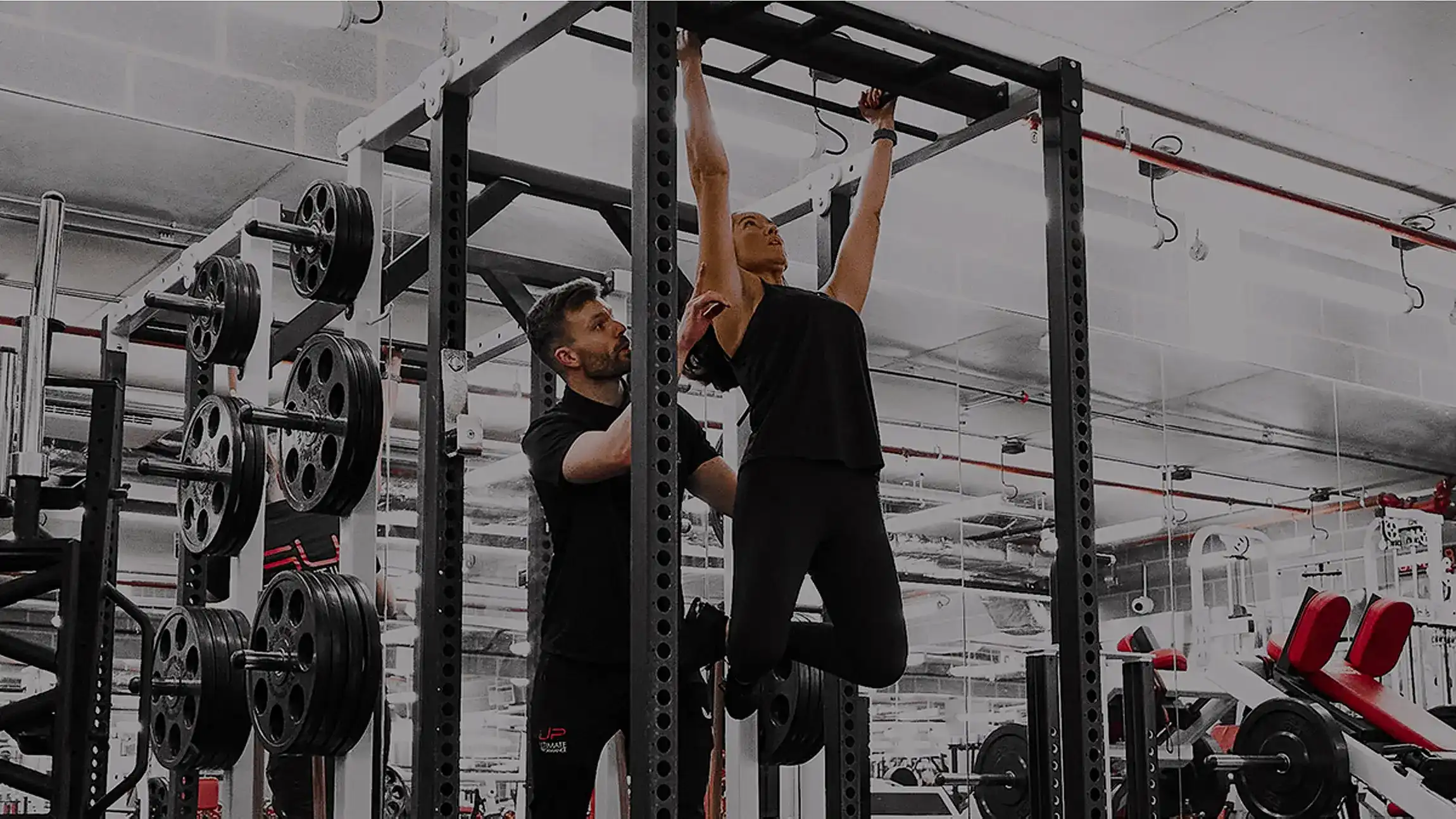 Woman doing pull-up exercise with a trainer assisting her in a gym.