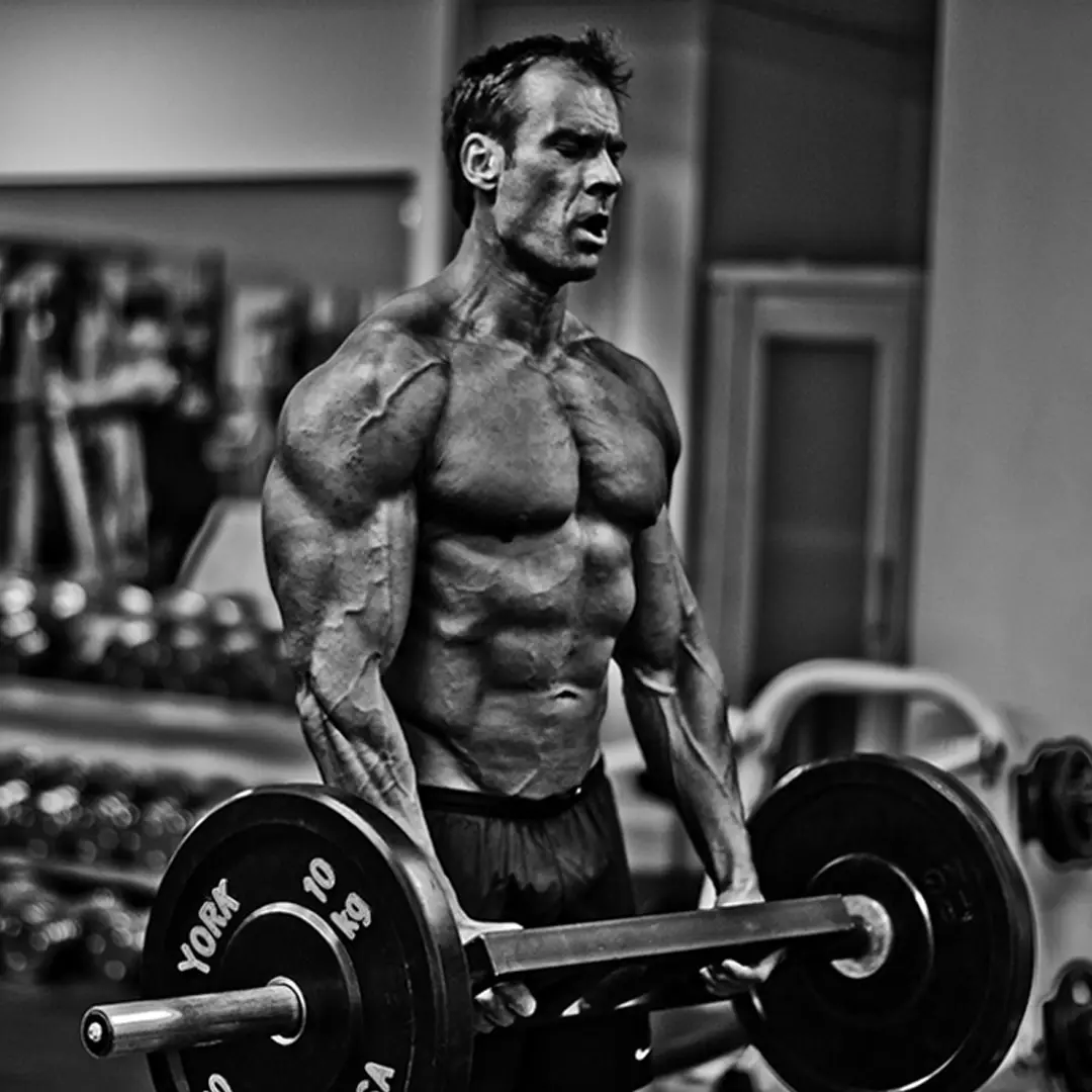 Muscular man lifting a barbell with 10 kg weights in a gym, showing intense effort.